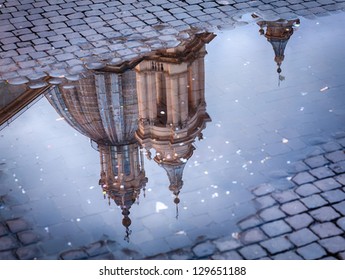 Sant Agnese in Agone lit up by setting sun in Piazza Navona reflected in puddle