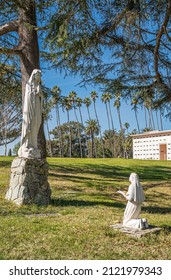 Santa Barbara, California, USA - February 8, 2022: Calvary Cemetery. Portrait, Our Lady of Lourdes statue group on green burial lawn. Smaller wall burial building and trees in back.