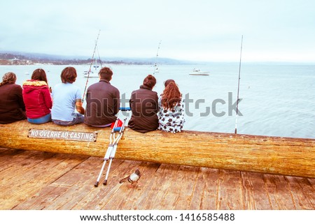 Santa Barbara pier, California. Group of relaxed friends or family members sit close together, fishing and watching blue sea waters of Pacific Ocean. Diversity in gender, age, disabilities and culture