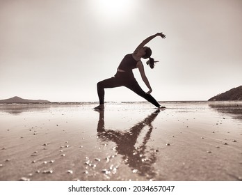 Santa Catarina, Brazil - Jul 2021: Woman in pants and black blouse practicing yoga on a deserted beach. The photograph is in sepia color.