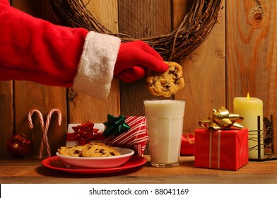 Santa Claus About To Dunk A Chocolate Chip Cookie Into A Glass Of Milk In A Rustic Old Fashioned Setting.