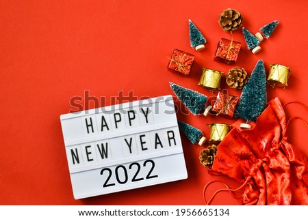 Santa Claus bag with decorative christmas toys and light box with text HAPPY NEW YEAR 2022 on a red background. Happy new year greeting card. 