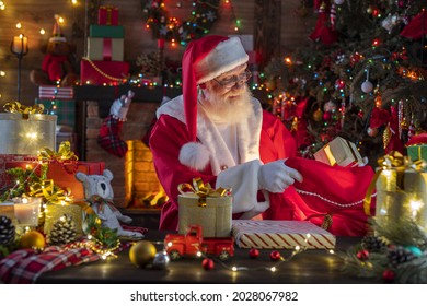 Santa Claus With A Bag With Presents Gifts Near Fireplace And Christmas Tree. Wooden House, New Year's Cheerful Mood Spirit Of Christmas. Senior Man With Real White Beard Cosplay Father Christmas.