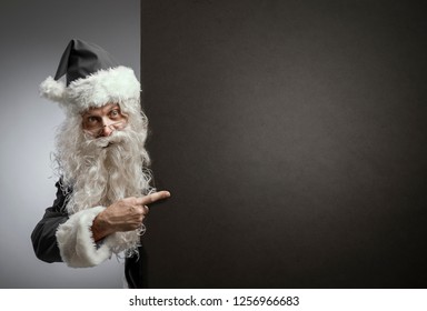 Santa Claus in black costume pointing at a blank sign, Black Friday commercial sign - Powered by Shutterstock