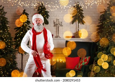 Santa Claus dancing near the fireplace and Christmas tree with gifts box, presents. New Year's cheerful mood Spirit of Merry Christmas. Senior man with real white beard cosplay Happy holidays concept
