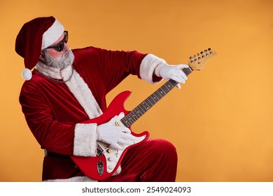 Santa Claus dressed in traditional red costume strumming red electric guitar against yellow background holding guitar playing posture celebrating festive spirit - Powered by Shutterstock