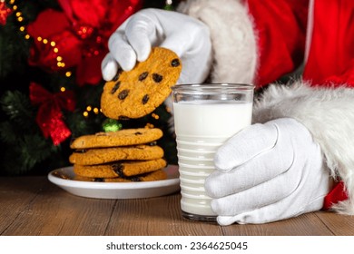 Santa Claus eating cookie and milk. Santa hands picking cookie and milk glass on wooden table against festive Christmas tree,  - Shutterstock ID 2364625045