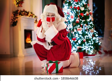 Santa Claus in face mask brings presents at Christmas tree and fireplace. Safe Xmas celebration during coronavirus outbreak. Winter holidays in covid-19 lockdown. Gifts for kids. - Powered by Shutterstock