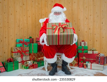 Santa Claus / Father Christmas Sitting In His Grotto Holding A Gift Wrapped Present For You.
