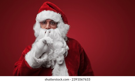 Santa Claus gesturing silence with finger on lips, mysterious holiday secret concept - Powered by Shutterstock