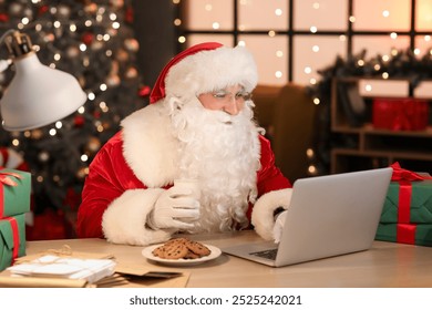 Santa Claus with glass of milk using laptop at home in evening - Powered by Shutterstock