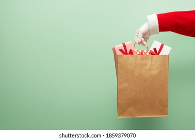 Santa Claus Hand Holding Brown Shopping Bag Paper With Gift Boxes On Green Isolated Background.