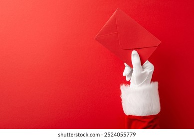 Santa Claus hand in a white glove holding a festive red envelope against a bright red background symbolizing Christmas spirit and celebrations - Powered by Shutterstock