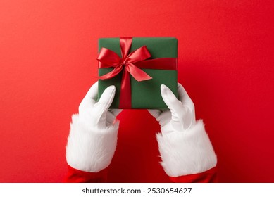 Santa Claus hands holding a green gift box with a red ribbon on a vibrant red background, representing Christmas celebration and gift giving - Powered by Shutterstock