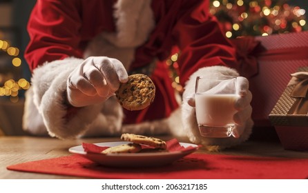 Santa Claus having a delicious snack, he is eating cookies and drinking milk, Christmas and holidays concept - Powered by Shutterstock
