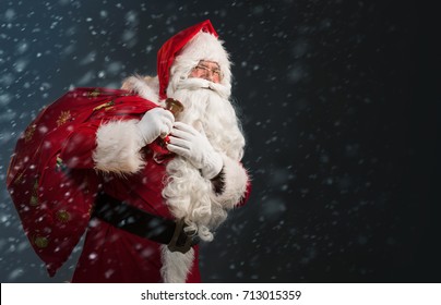 Santa Claus holding a bag with presents and ringing a bell on a dark background with snow 