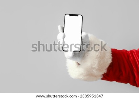 Santa Claus holding mobile phone with blank screen on grey background