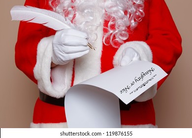 Santa Claus Holding A Quill Pen Whilst Checking The Naughty Or Nice List.