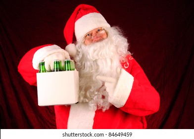 Santa Claus Holding A Six Pack Of Beer Bottles. Horizontal Format With A Maroon Fabric Background