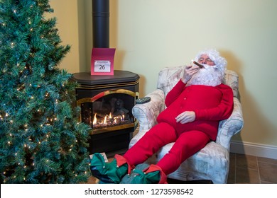 Santa Claus In House Enjoying A Celebratory Cigar In Easy Chair Wearing Red Long Johns Relaxing The Day After Christmas.