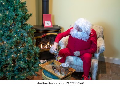 Santa Claus In House Mixing Martini In Front Of Fire Wearing Red Long Johns Relaxing The Day After Christmas.