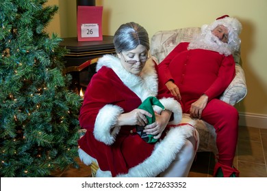 Santa Claus In House Wearing Red Long Johns Getting Relaxing Foot Massage From The Mrs On  The Day After Christmas.