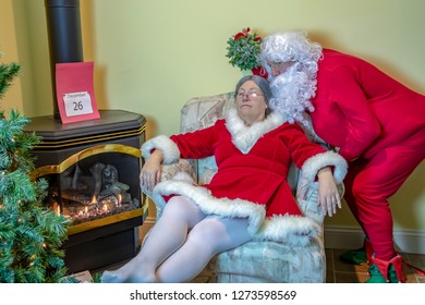 Santa Claus In House Wearing Red Long Johns Sneaking Up On The Mrs. With Mistletoe  The Day After Christmas.