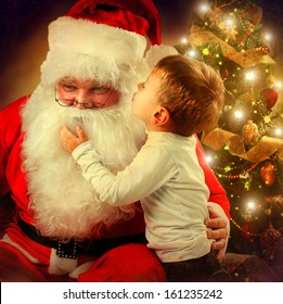 Santa Claus and Little Boy. Christmas Scene. Boy Telling Wish in Santa Claus's Ear in front of Christmas Tree  - Powered by Shutterstock