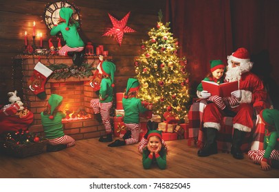 Santa Claus and little elves before Christmas in his house by fireplace and Christmas tree