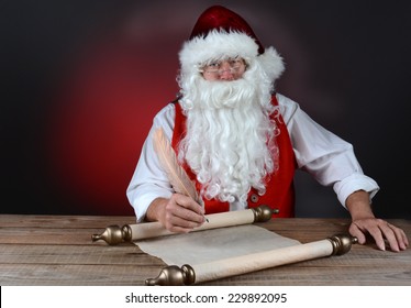 Santa Claus Making His Naught And Nice List On A Scroll Of Parchment Paper. Santa Is Seated At A Rustic Wood Table. Horizontal Format On Light To Dark Red Background.