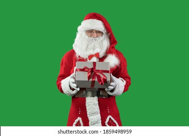 santa claus on a green background holding a box wrapped in craft paper. Red ribbon and bow. Copy space.