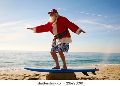 Santa Claus Practices His Surfing Skills On His Surf Board On The Beach, Before He Goes Into The Ocean. Santa Loves The Beach When On Vacation From Delivering Gifts To Good Boys And Girls At Christmas