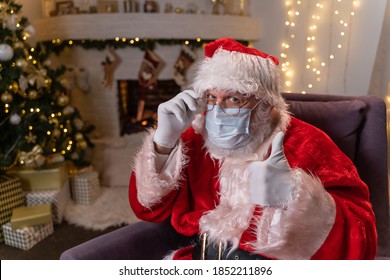 Santa Claus in a protective medical mask while sitting in a chair by the fireplace and Christmas tree. Covid 19, protection against coronavirus. - Powered by Shutterstock