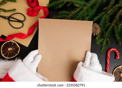 Santa Claus Reading Letters from Children on Desk. Top View of Jolly Father Hands Holding a Blank Brown Paper Page. View from Above of Wood Table with Ornament, Christmas Decoration. Letter Mock Up - Powered by Shutterstock