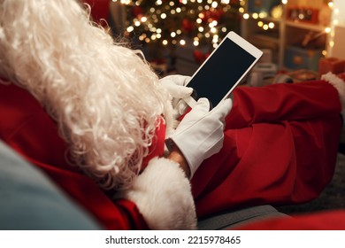 Santa Claus relaxing on the couch and connecting with his digital tablet at Christmas - Powered by Shutterstock