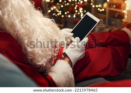 Santa Claus relaxing on the couch and connecting with his digital tablet at Christmas
