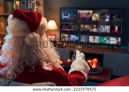 Santa Claus relaxing on the couch at home and watching TV, he is choosing a movie on the video on demand menu