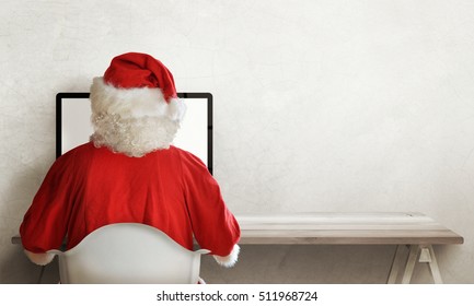 Santa Claus responds to letter of wishes on a computer. Front view of Santa Claus office. Free space for text on right side. White wall in background.