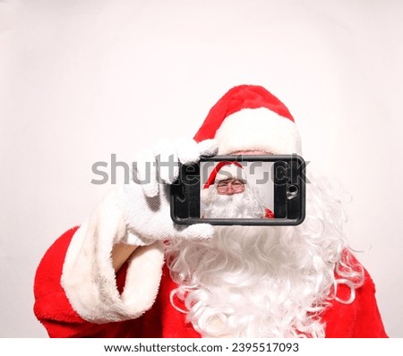 Santa Claus Selfie. Santa Claus taking a selfie with a cell phone. Chris Cringle taking a Selfie Photo with his Cell Phone for Christmas Pictures. Happy Santa Claus doing a Video Chat with his Phone.