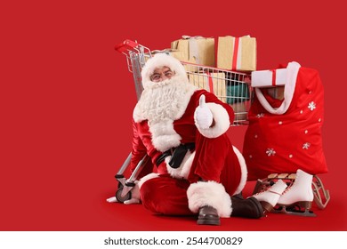 Santa Claus showing thumb-up gesture with ice skates, bag and shopping cart with gift boxes on red background. Christmas celebration - Powered by Shutterstock