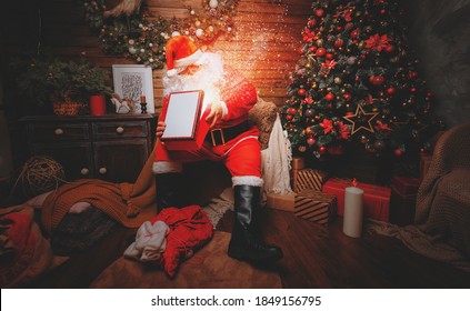 Santa Claus sits in a chair inside of his house and open box with gifts for christmas greetings. Beautiful home decoration  