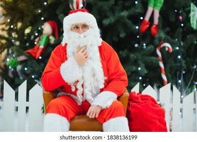 Santa Claus Sitting On A Chair Near The Christmas Tree In The Mall