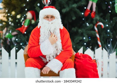 Santa Claus Sitting On A Chair Near The Christmas Tree In The Mall