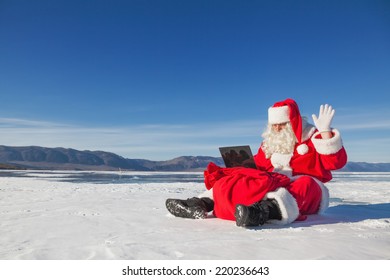 Santa Claus sitting on snow, looking at laptop news, shooting was conducted in a sunny day on lake Baikal