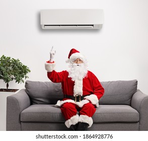 Santa Claus Sitting On A Sofa And Pointing To An Air Conditioning Unit Above Mounted On The Wall