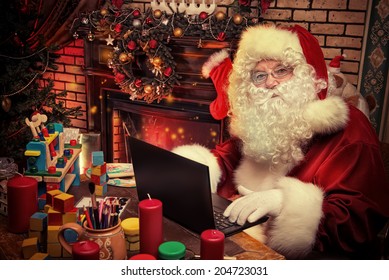 Santa Claus Sitting At The Table With A Laptop At His Home. Christmas Time.