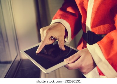 Santa Claus Standing At Window And Using Apps Resize On A Touch Screen Tablet, Christmas And Technology Concept