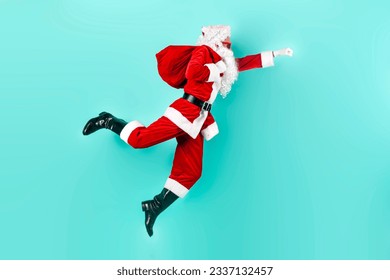 santa claus in suit with bag of gifts jumps and quickly runs in the air on blue isolated background, santa flies and hurries for the new year and christmas - Powered by Shutterstock