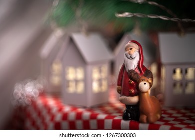 Santa Claus Toy With His Deer Rudolf On The Background Of New Year's Garland Of Houses