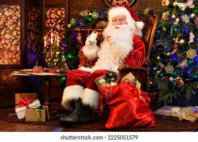 Santa Claus in a traditional costume with a bag of gifts by the fireplace